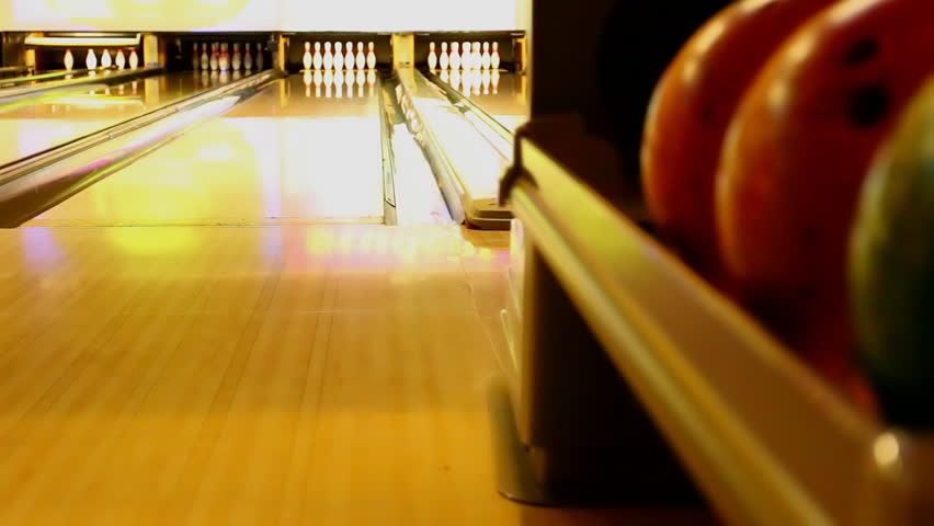 Man picks an orange bowling ball and bowls a strike knocking down all ten pins. HD stock