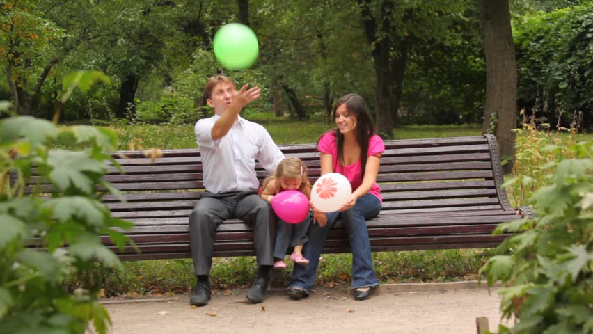 Happy Family Throws Balloons Sitting On Brown Bench In Happy Family Throws Balloons Sitting On Brown Bench In