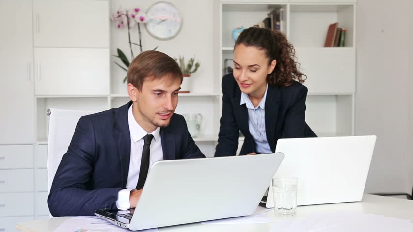 Two Business People Working While Sitting At A Desk In A Bright Office ...