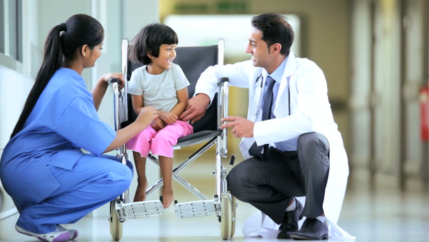 Nurse And Doctor Reassuring Cute Indian Child In A Wheelchair Waiting ...